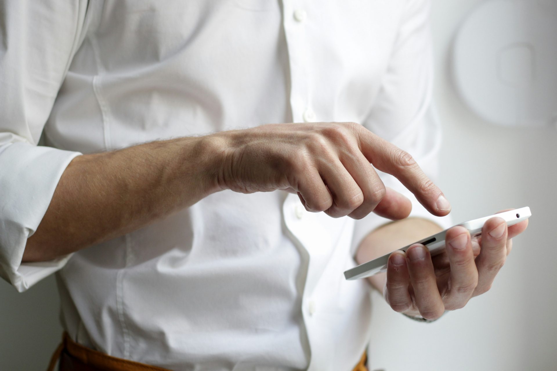 Personne portant une chemise blanche et tenant un smartphone Android blanc.